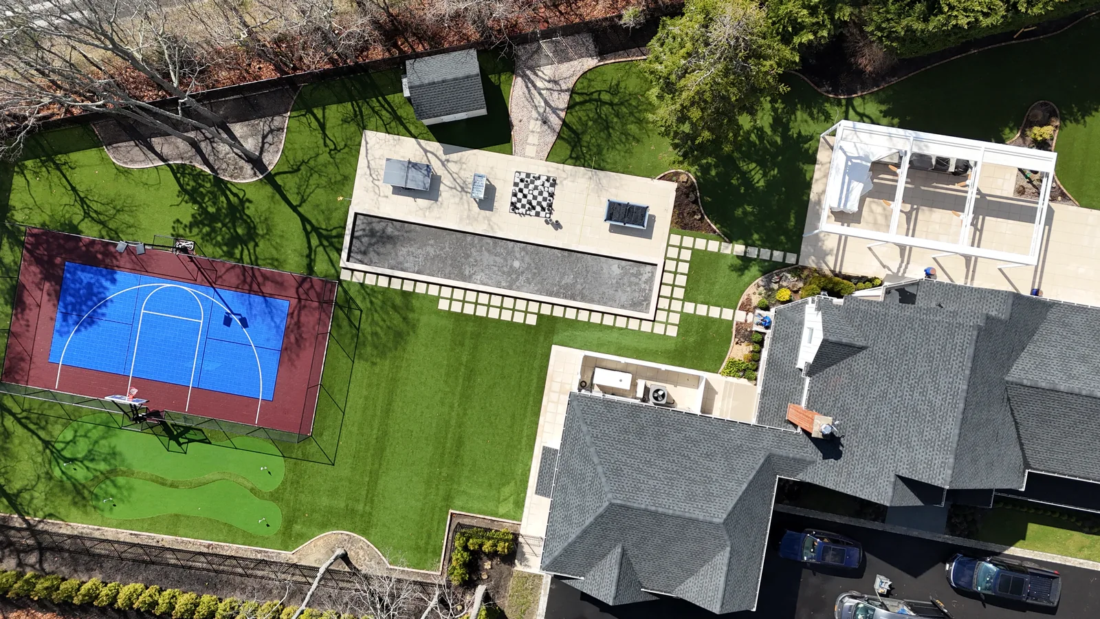 Aerial view of a property with stone patio, pool, turf lawn, and court