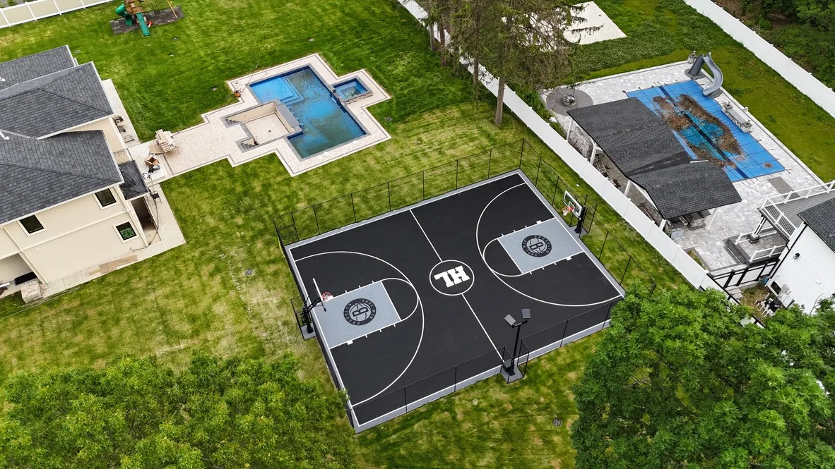 Black full court with a white center court logo, fencing, and two hoops