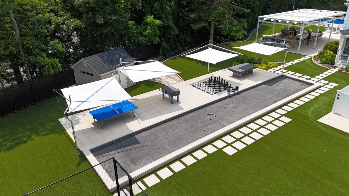 The same gaming area with the four sail shades extended, throwing shade across the ping pong table and patio