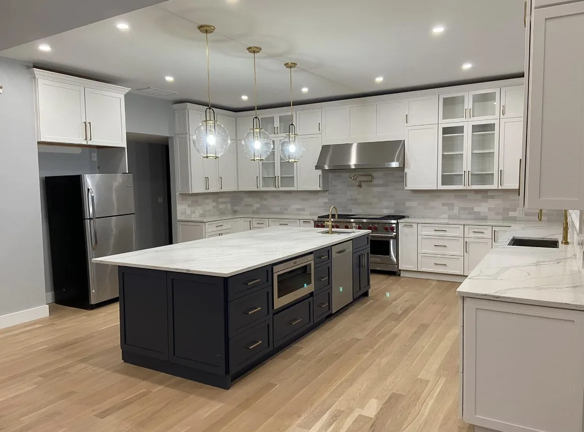 Renovated kitchen with white shaker cabinets, a navy island with a marble top, brass pendant lights and a stainless range with a tile backsplash