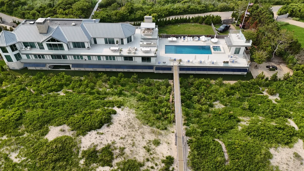 Aerial view of the finished oceanfront property: green turf and planting around the pool deck, with the boardwalk running out over the dune