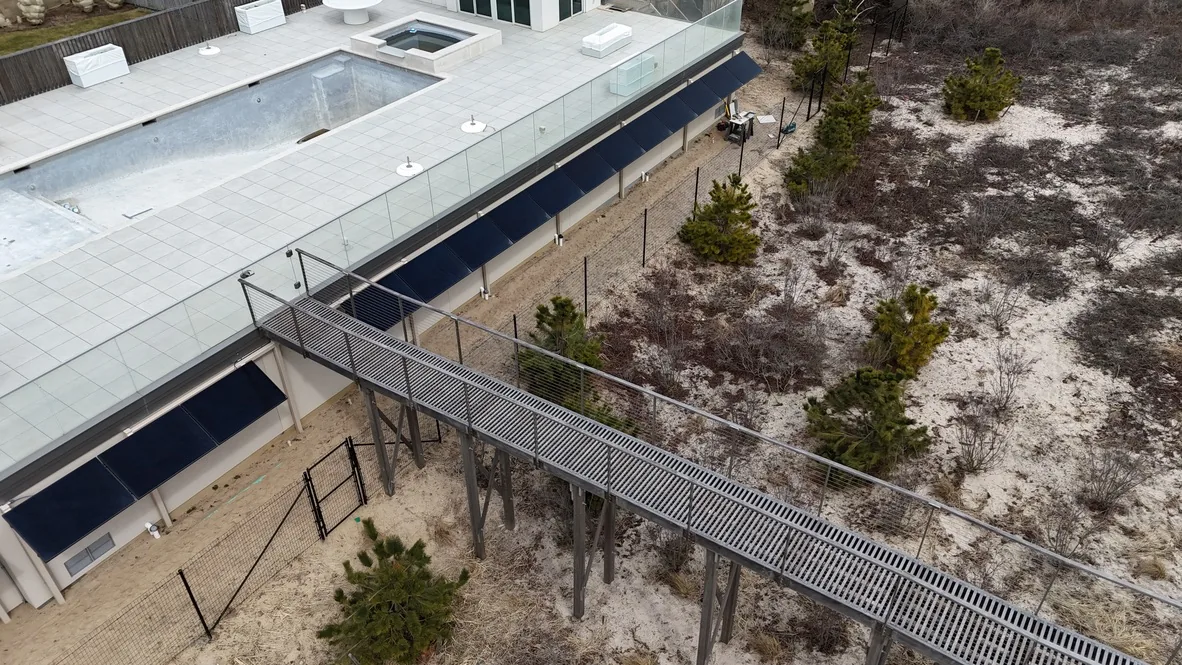 Aerial view of the oceanfront property before the turf went in: bare sand, construction fencing, and an unfinished pool beside the boardwalk