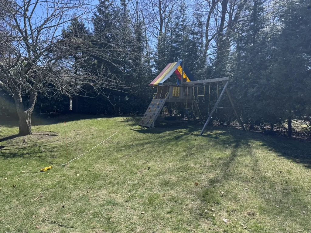 The same backyard before the build: lawn with a wooden swing set and a string line marking out the court footprint