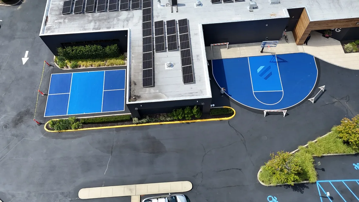 The same lot with a blue pickleball court and a blue basketball half court laid into the surface, with new planting beds along the edge